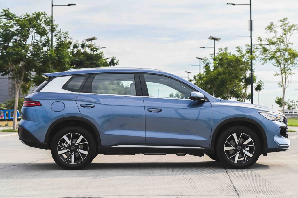 Side profile of the BYD Sealion 5 DM-i in Deep Sea Blue, parked on a concrete lot with trees and lamp posts in the background.