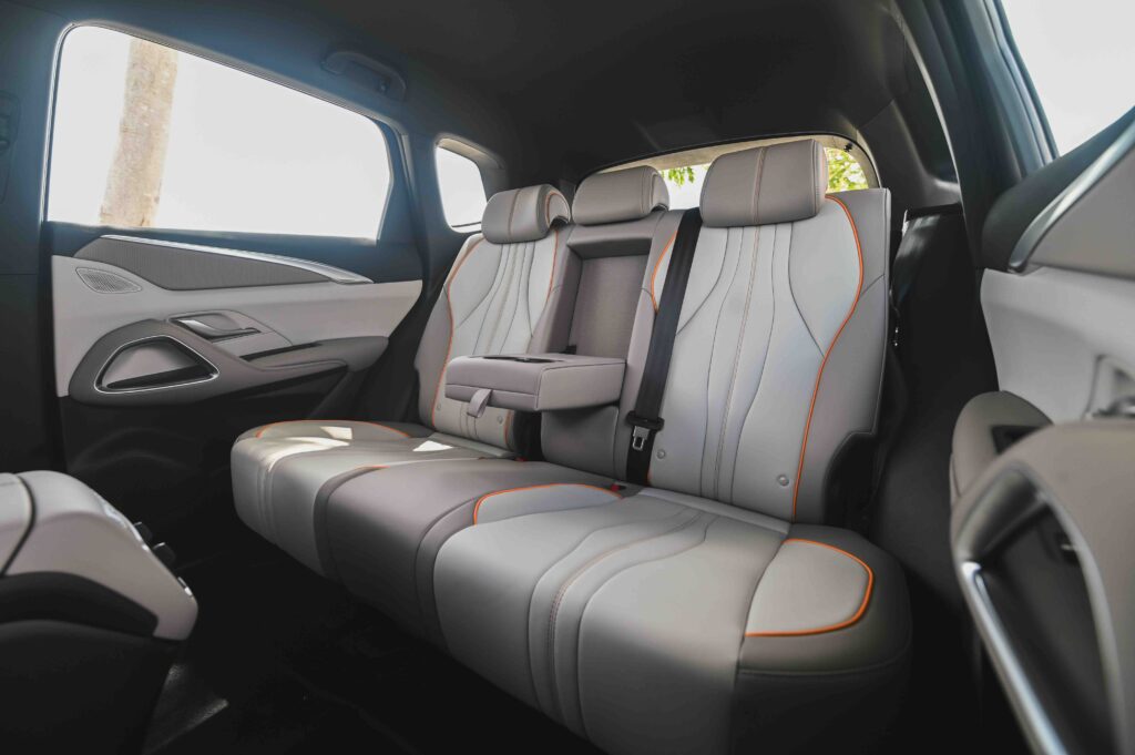 Rear seats of the BYD Sealion 5 DM-i shown in beige leather with orange piping, foldable center armrest, and premium door panel finishes.