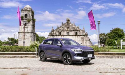 A BYD Sealion 5 DM-i in Deep Sea Blue is parked in front of the historic Paoay Church in Ilocos Norte, with pink flags waving in the background under a bright blue sky.