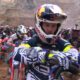 Manuel Lettenbichler, wearing a Red Bull helmet and racing gear, prepares at the starting line of the 2025 Red Bull Erzbergrodeo with a focused expression. Behind him, a sea of fellow riders on dirt bikes waits in anticipation amid the rugged quarry backdrop of Eisenerz, Austria.