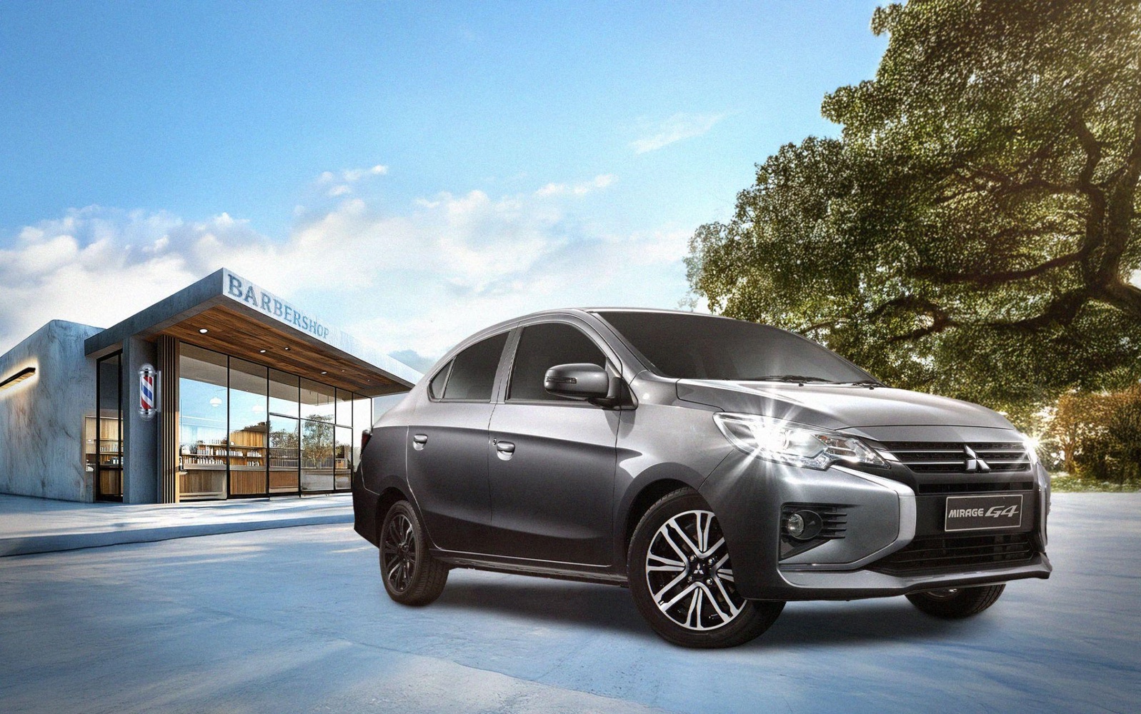 A sleek gray Mitsubishi Mirage G4 sedan is parked in front of a modern barbershop with a large glass window and a sign reading "BARBERSHOP." The scene features a clear blue sky with scattered clouds and a large tree with lush green foliage, creating a bright and inviting atmosphere.