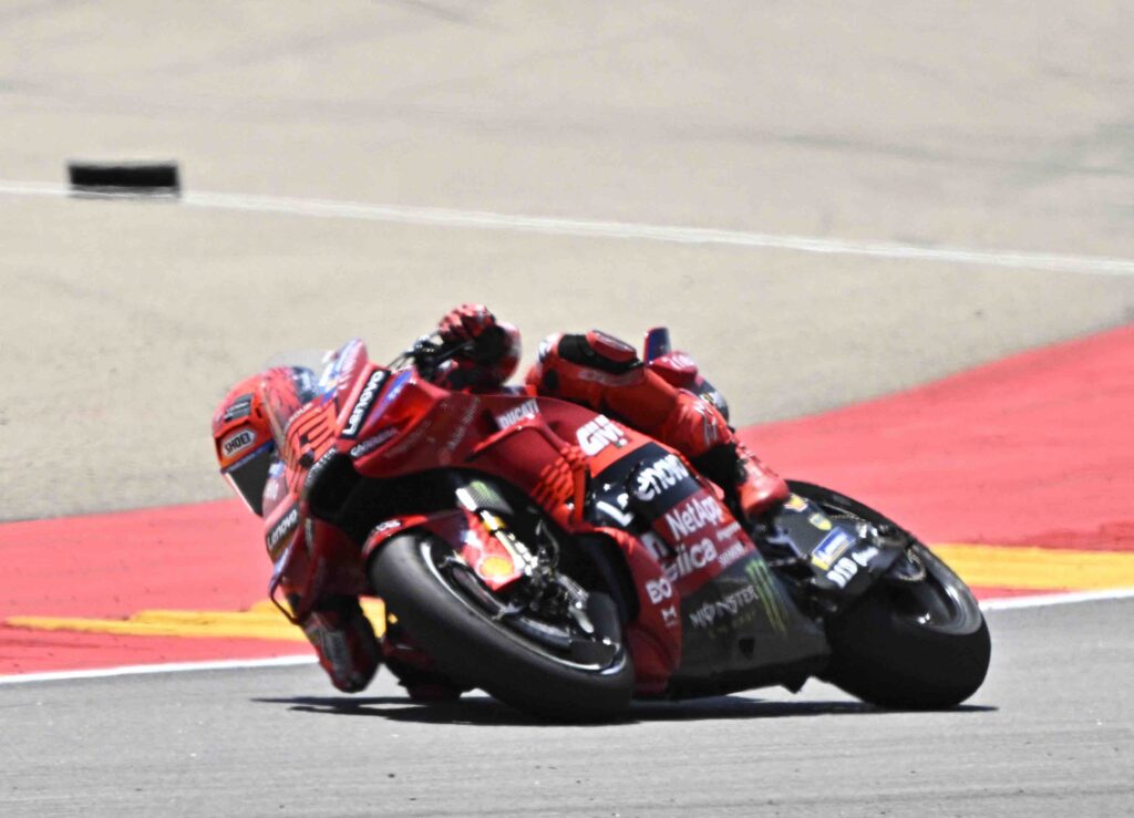 Marc Marquez leans sharply into a turn on his red Ducati during the Aragon MotoGP, fully tucked behind the windscreen as the bike carves through the corner on a sunlit track.