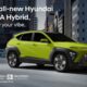 A vibrant lime-green Hyundai KONA Hybrid drives along an elevated city road surrounded by tall, modern buildings at dusk. The car’s futuristic design is highlighted by LED headlights, bold lines, and contrasting black wheel arches, capturing its dynamic urban character.