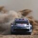 A Toyota GR Yaris Rally1 kicks up a massive cloud of dust as it powers through a gravel corner during the 2024 Rally of Sardinia. The car, bearing Sebastien Ogier’s number and Red Bull branding, displays dirt and grit from the intense competition.