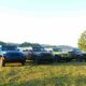 A lineup of colorful Jeep® Wrangler 4-Door models parked on a grassy field beside a lake, with hills and trees in the background under a clear sky.