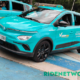 A brightly colored Green GSM electric taxi, a VinFast Nerio EV, is parked at a launch event in Quezon City. The car features a sleek cyan body with black rims and the Green GSM hotline visibly printed on the door. A driver sits inside while another e-taxi is seen beside it.