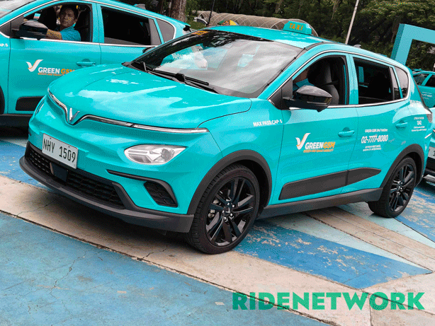 A brightly colored Green GSM electric taxi, a VinFast Nerio EV, is parked at a launch event in Quezon City. The car features a sleek cyan body with black rims and the Green GSM hotline visibly printed on the door. A driver sits inside while another e-taxi is seen beside it.