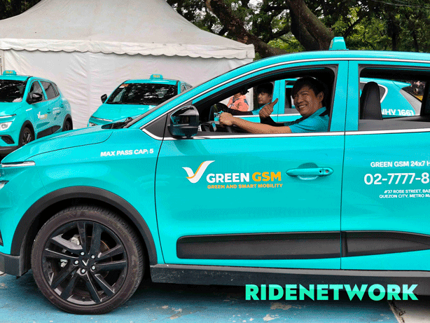 A Green GSM driver smiles from the driver’s seat of a VinFast Nerio EV taxi at the launch event in Quezon City. Behind him, other drivers give a thumbs-up from their electric taxis, all in the brand’s signature cyan color. The RIDENETWORK watermark appears on the lower right corner.
