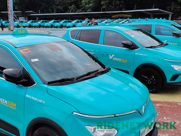 Rows of brand-new Green GSM VinFast Nerio EV taxis are lined up in perfect formation at the launch venue in Quezon City. The taxis, in their iconic cyan color with "TAXI" signs and visible hotline decals, stretch deep into the background. The RIDENETWORK watermark is placed at the bottom right.