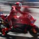 A red-clad MotoGP rider on a Ducati bike streaks past the pit lane, captured with dramatic motion blur.