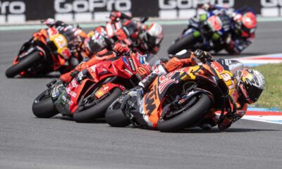 MotoGP riders leaning into a high-speed corner during the Czech Sprint Race, led by KTM and Ducati bikes with multiple riders close behind.