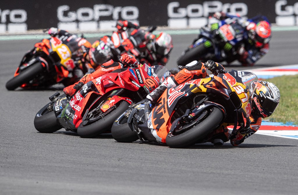 MotoGP riders leaning into a high-speed corner during the Czech Sprint Race, led by KTM and Ducati bikes with multiple riders close behind.
