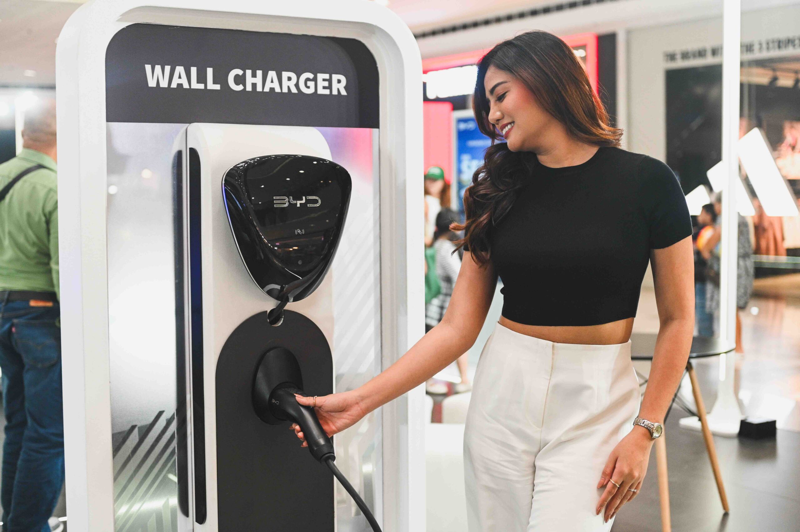 Woman smiling while holding the plug of a BYD electric vehicle wall charger at an indoor exhibit. Let me know if you need more images captioned or want to feature this on your site or socials!