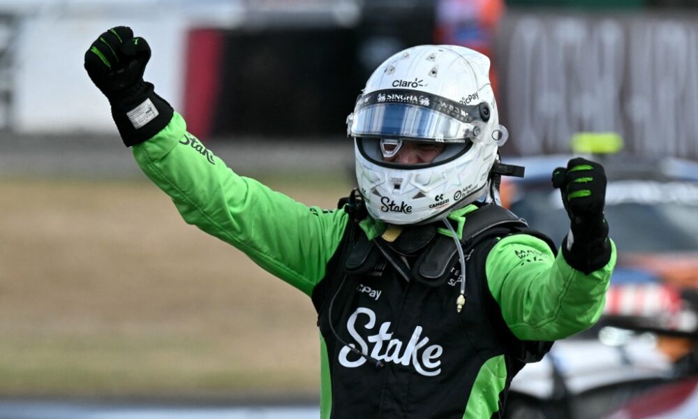 Nico Hulkenberg in green-and-black racing gear raises his fists in celebration after securing third place at the 2025 British Grand Prix.