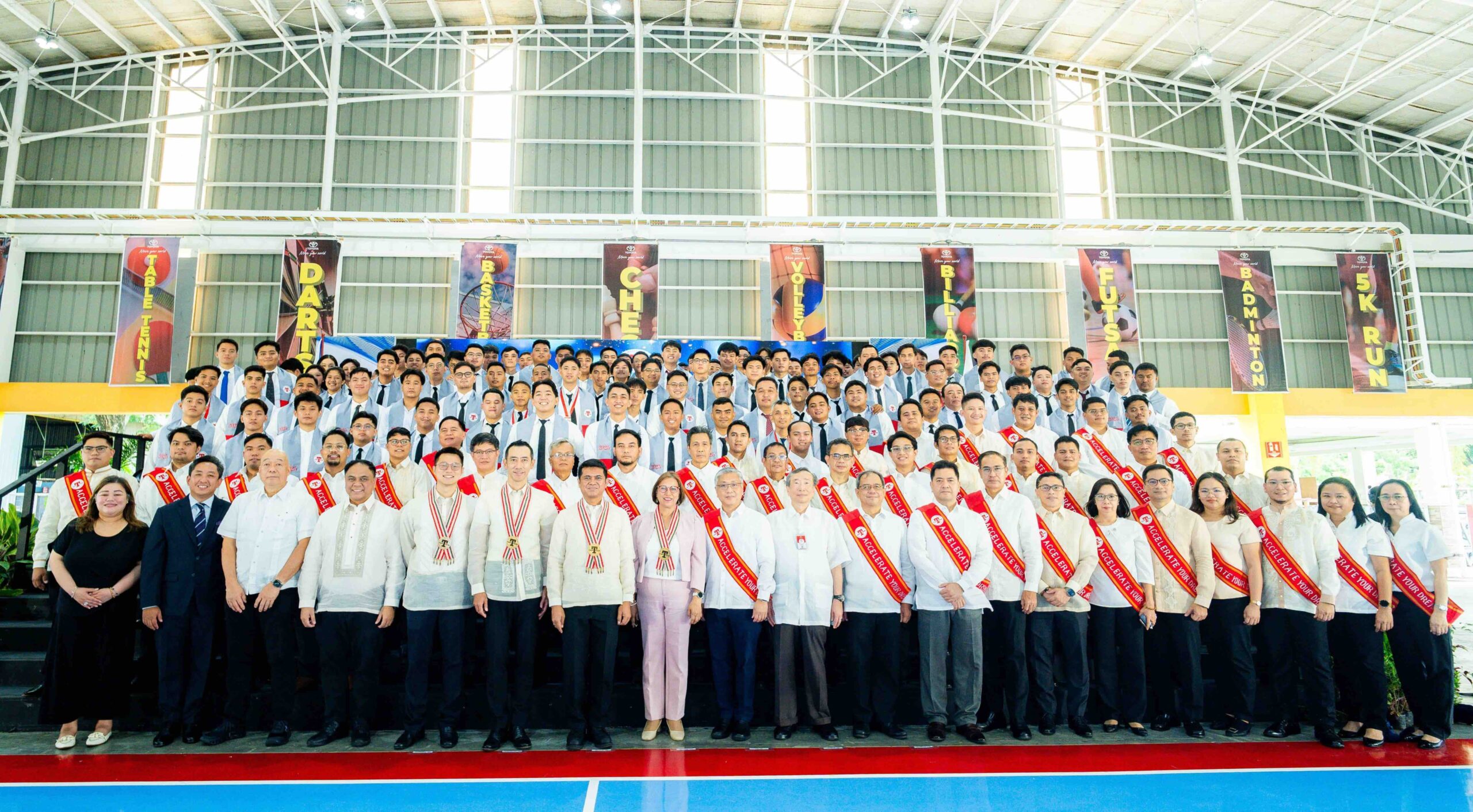 A large group photo of TMP Tech graduates and faculty members posing indoors during the 14th commencement ceremony, with graduates wearing sashes and formal attire.