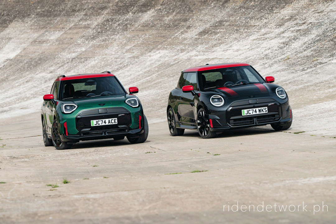 Two all-new MINI John Cooper Works models—an Aceman in Rebel Green and a 3-door Electric in Midnight Black—driving side by side on a steeply banked concrete track.