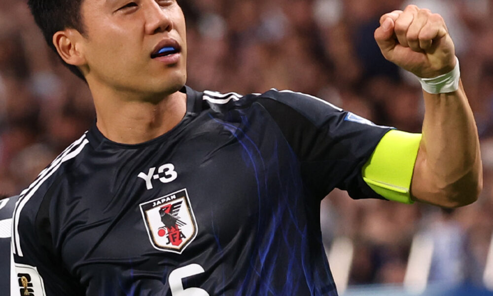 Wataru Endo, captain of Japan’s national football team, pumps his fist in celebration while wearing the team's dark blue kit and captain's armband during a match.