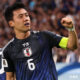 Wataru Endo, captain of Japan’s national football team, pumps his fist in celebration while wearing the team's dark blue kit and captain's armband during a match.