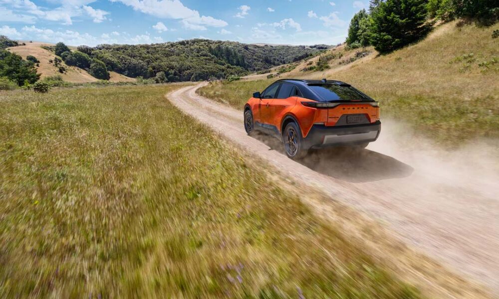 2026 Subaru Uncharted in orange driving on a dusty off-road trail through grassy hills under a bright blue sky.