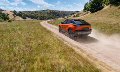 2026 Subaru Uncharted in orange driving on a dusty off-road trail through grassy hills under a bright blue sky.