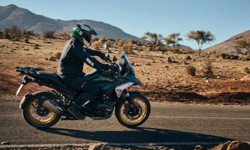 Rider on a BMW R 1300 GS Option 719 motorcycle traversing a desert road with mountainous terrain in the background.