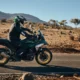 Rider on a BMW R 1300 GS Option 719 motorcycle traversing a desert road with mountainous terrain in the background.