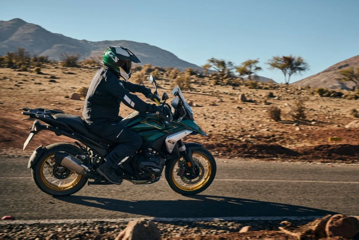 Rider on a BMW R 1300 GS Option 719 motorcycle traversing a desert road with mountainous terrain in the background.