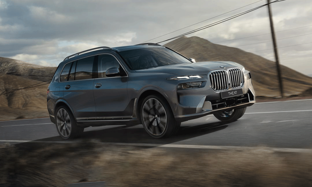 BMW X7 xDrive40d luxury SUV driving on a winding mountain road under a cloudy sky.