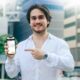Man in white shirt smiles and points to a smartphone showing the Shell Recharge station on the Evro app.