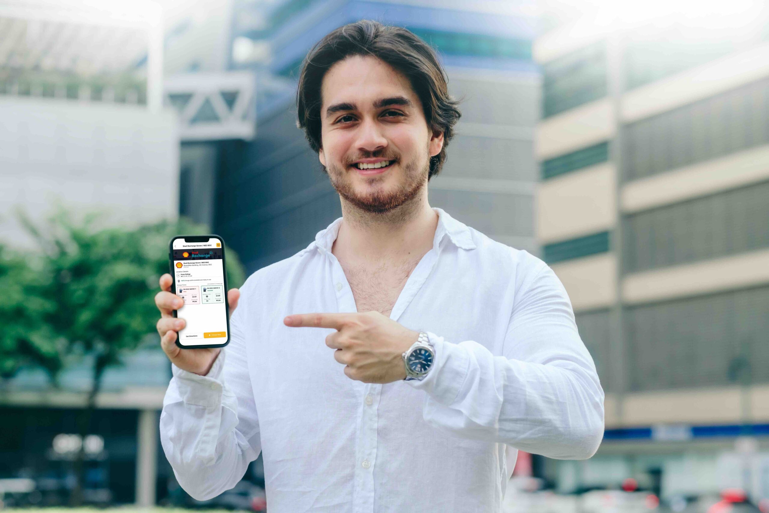 Man in white shirt smiles and points to a smartphone showing the Shell Recharge station on the Evro app.
