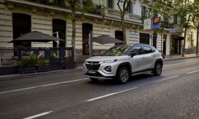 Silver Suzuki Fronx GLX compact SUV driving along a city street lined with outdoor cafes and historic buildings