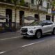Silver Suzuki Fronx GLX compact SUV driving along a city street lined with outdoor cafes and historic buildings
