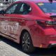 Rear side view of a red Honda City with “Honda Sensing City” graphics parked in a sunlit lot.