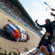 Hyundai N team members cheer and wave flags at the pit wall as the ELANTRA N TCR race car crosses the finish line at the Nürburgring 24-hour endurance race, celebrating a hard-fought victory under bright skies and a packed grandstand.