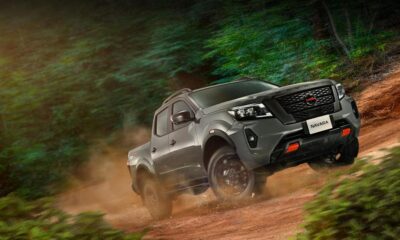 A Nissan Navara PRO-4X drives off-road through a forest trail, kicking up dirt as it climbs a rugged slope.