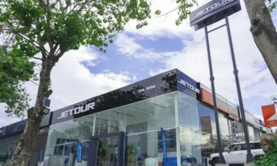 Exterior view of the newly opened Jetour Auto Santa Rosa dealership, featuring a sleek glass showroom, Jetour signage, and a tree-lined street under a partly cloudy sky.