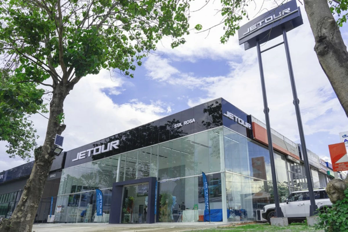 Exterior view of the newly opened Jetour Auto Santa Rosa dealership, featuring a sleek glass showroom, Jetour signage, and a tree-lined street under a partly cloudy sky.