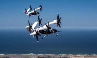 Two Joby electric air taxis in mid-flight over a coastal landscape, demonstrating their vertical takeoff and landing capabilities.