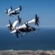 Two Joby electric air taxis in mid-flight over a coastal landscape, demonstrating their vertical takeoff and landing capabilities.