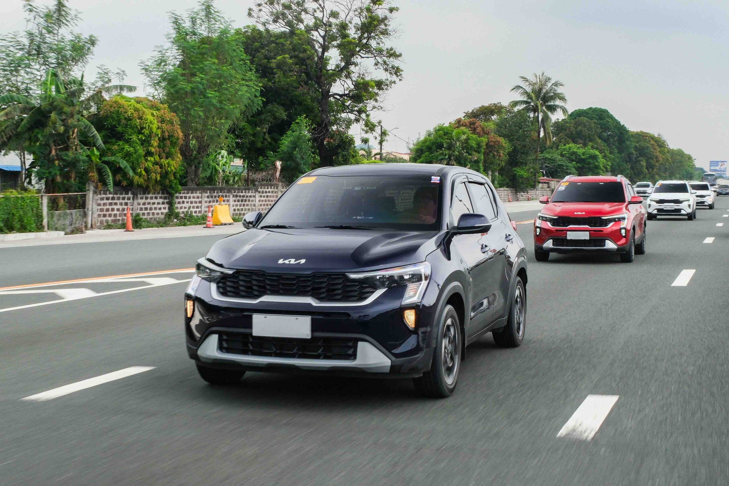 A convoy of Kia Sonet SUVs cruises along a highway, led by a black unit followed by red and white Sonets, during the Kia Sonet Pilipinas Club’s grand meet in Nuvali.