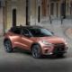 A copper-colored Lexus LBX compact crossover parked on a European-style cobblestone street, featuring sleek headlights, black roof, and sporty alloy wheels.
