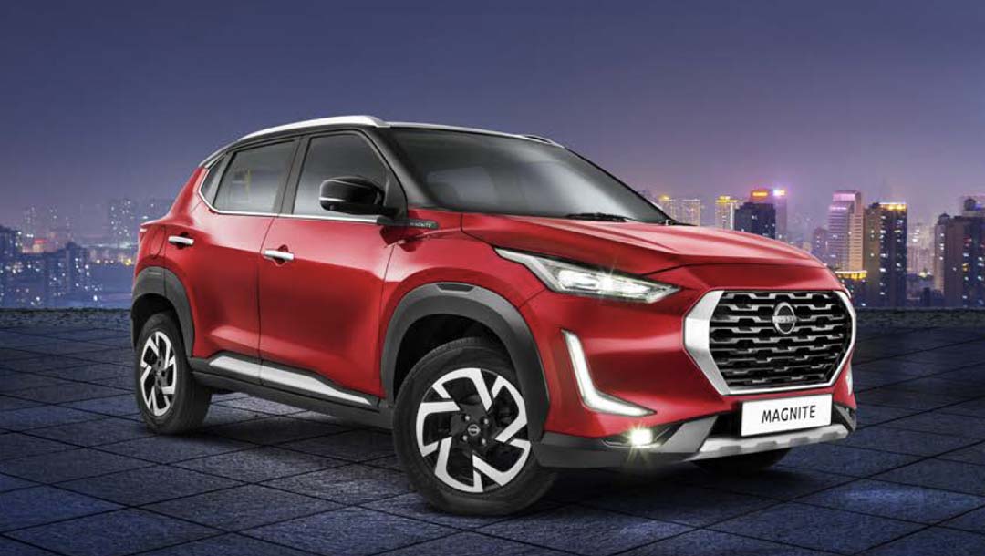 A red Nissan Magnite subcompact crossover parked on a tiled rooftop with a city skyline at night.