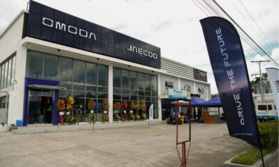 A newly opened Omoda and Jaecoo dealership with a modern glass façade, flower stands at the entrance, and “Drive the Future” banners outside.
