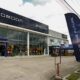 A newly opened Omoda and Jaecoo dealership with a modern glass façade, flower stands at the entrance, and “Drive the Future” banners outside.