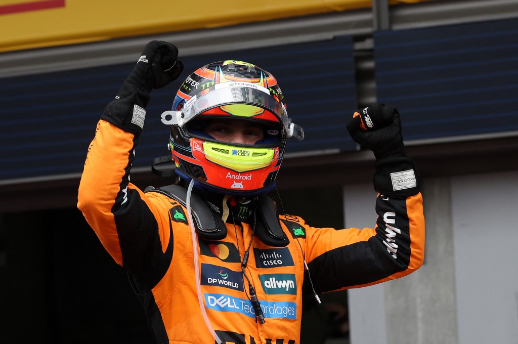 Oscar Piastri celebrates with raised fists while wearing his McLaren racing suit and helmet after winning the Belgian Grand Prix.