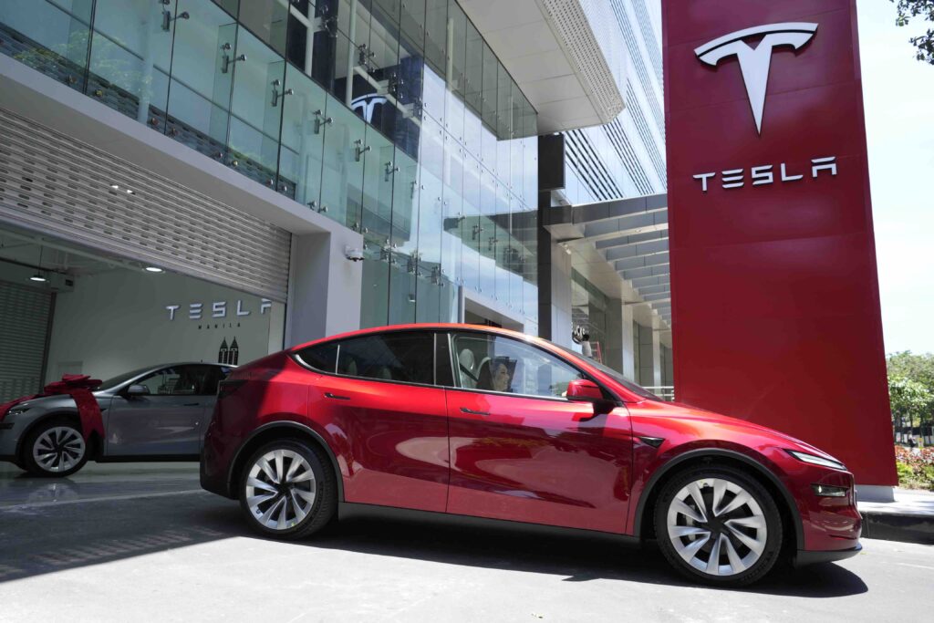 Red Tesla Model Y parked outside Tesla Manila showroom in bright daylight.