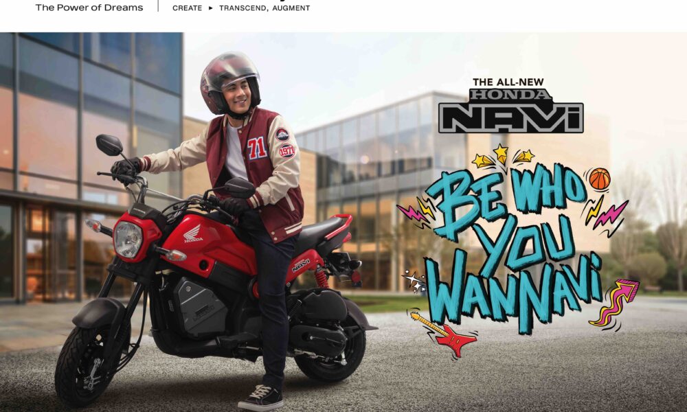 Young man in red varsity jacket sitting on a red Honda NAVi scooter, smiling confidently outside a modern building with “Be Who You WANNAVi” text beside him.