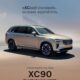 A beige Volvo XC90 T8 Ultra Plug-in Hybrid SUV parked on a minimalistic, desert-toned landscape with soft lighting and a pastel gradient sky. Text reads: “eXCeed standards. surpass aspirations.”