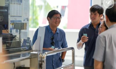 President Ferdinand Marcos Jr. smiles while talking to passengers at a train station booth, holding a fare card, alongside other individuals.