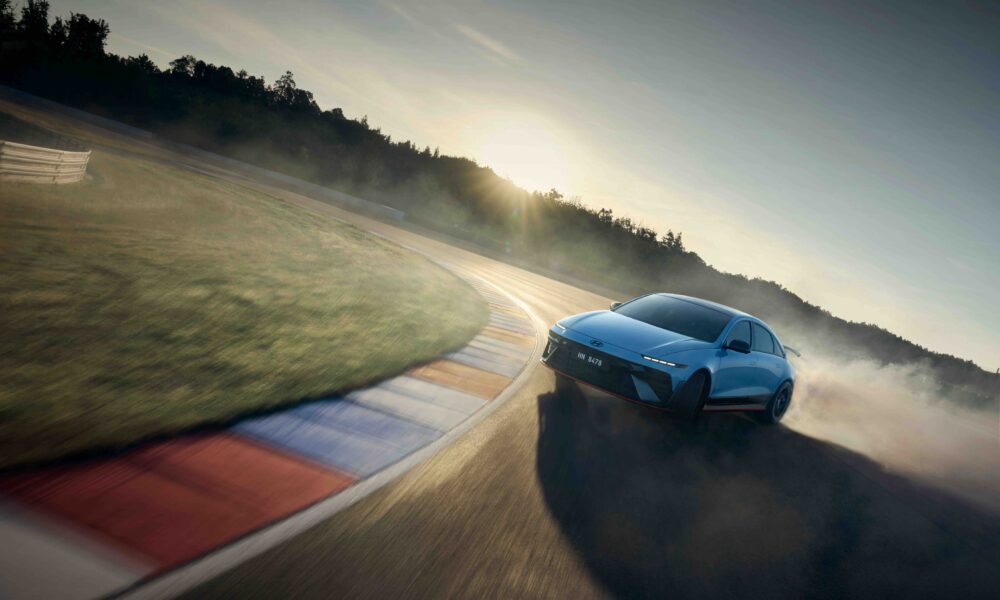 A Hyundai IONIQ 6 N powerslides around a racetrack corner at sunset, kicking up smoke and showcasing its performance handling.